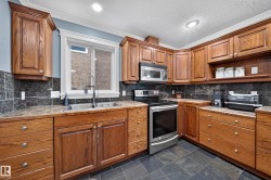 Full kitchen featuring wood cabinetry, stainless steel appliances, dark tile flooring, and a large window above the sink - 
