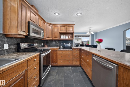 Wood-finish cabinetry, stainless steel appliances, dark stone-finish countertops, black tile backsplash, and slate-finish flooring - 6904 18 Avenue Sw, Edmonton, AB 