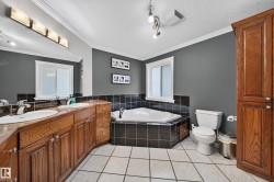 Dual vanity with wood-finish cabinetry, built-in corner bathtub with tile surround, white tiled flooring, and crown molding - 