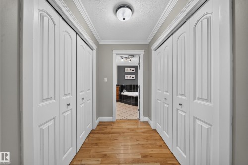 Wood-finish flooring, white bi-fold closet doors, crown molding, flush mount lighting, and a tiled bathroom floor - 6904 18 Avenue Sw, Edmonton, AB 