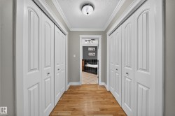 Wood-finish flooring, white bi-fold closet doors, crown molding, flush mount lighting, and a tiled bathroom floor - 