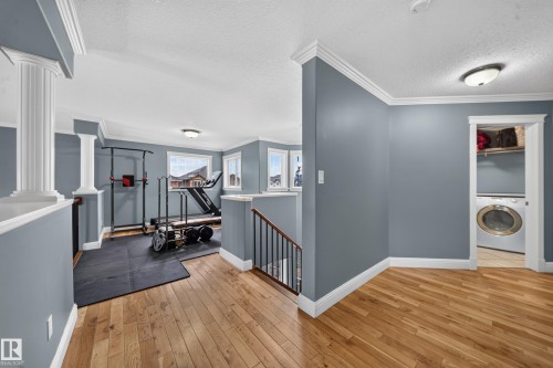 Light wood-finish flooring, white crown molding, accent columns, and a built-in laundry area with a washing machine and shelving - 6904 18 Avenue Sw, Edmonton, AB 