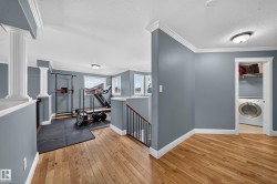 Light wood-finish flooring, white crown molding, accent columns, and a built-in laundry area with a washing machine and shelving - 
