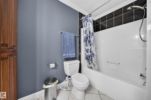 Built-in wood-finish cabinetry, white toilet, white bathtub with integrated grab bar, black subway tile shower surround, and tile flooring - 6904 18 Avenue Sw, Edmonton, AB 