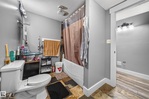 Bathroom featuring a built-in tub and shower combination, a toilet, and multi-toned tile flooring - 6904 18 Avenue Sw, Edmonton, AB 