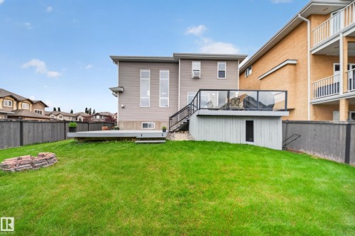 Expansive backyard featuring a manicured lawn, a raised deck with glass railings, and a ground-level patio - 6904 18 Avenue Sw, Edmonton, AB 