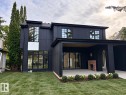 Modern dark-panel exterior featuring an expansive concrete patio, multiple large grid-pattern windows, a covered outdoor living area, and an integrated brick outdoor fireplace - 10414 134 Street Nw, Edmonton, AB 