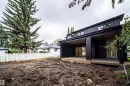 Modern black exterior with a sloped roofline, featuring two covered patios with recessed lighting, a white picket fence, and mature evergreen trees - 10414 134 Street Nw, Edmonton, AB 