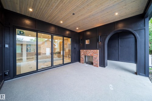 Covered patio featuring a wood-panel ceiling with recessed lighting, brick fireplace, black wall paneling, and an arched entry - 10414 134 Street Nw, Edmonton, AB 