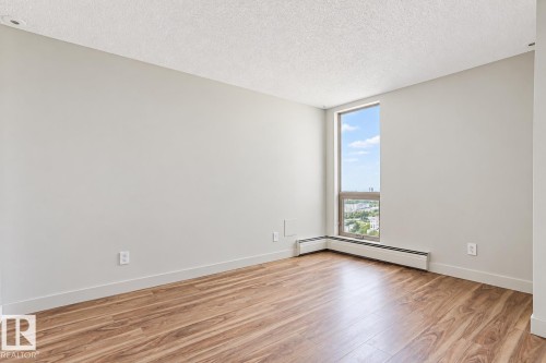 Wood-finish flooring, light grey painted walls, window with aluminum frame, white baseboard heating, and textured ceiling - #2005 10149 Saskatchewan Dr Nw, Edmonton, AB 