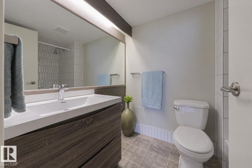 Modern bathroom featuring a floating vanity with an expansive white countertop, wood-finish cabinetry, and chrome faucet fixtures - #2005 10149 Saskatchewan Dr Nw, Edmonton, AB 