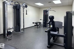 Fitness facility featuring multiple weight machines, padded flooring, and fluorescent overhead lighting - 