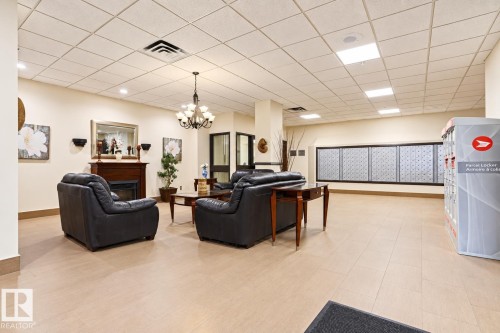Lounge area with light-toned flooring, featuring a classic fireplace, a decorative chandelier, and recessed lighting - #2005 10149 Saskatchewan Dr Nw, Edmonton, AB 