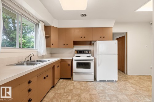 Kitchen featuring a double basin stainless steel sink, laminate countertops, wood-finish cabinetry, and a window with outdoor scenery - 12424 77 Street Nw, Edmonton, AB 