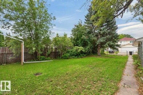 Expansive green lawn framed by mature trees and a wood-panel fence - 12424 77 Street Nw, Edmonton, AB 