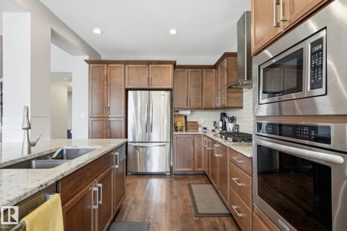 Gourmet kitchen featuring stainless steel appliances, wood-finish flooring, light-toned countertops, subway tile backsplash, and extensive wood cabinetry - 3204 Abbott Crescent Sw, Edmonton, AB - Indoor Photo Showing Kitchen With Upgraded Kitchen