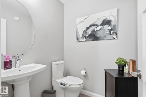 Pedestal sink with chrome fixtures and a circular mirror - 3204 Abbott Crescent Sw, Edmonton, AB - Indoor Photo Showing Bathroom