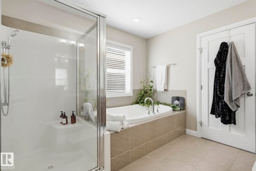 Bathroom featuring a tiled soaking tub surround, a built-in tub, a window with blinds, a glass-enclosed shower, and light-toned tile flooring - 3204 Abbott Crescent Sw, Edmonton, AB - Indoor Photo Showing Bathroom