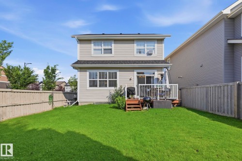 Expansive fenced backyard featuring a manicured lawn, a two-story residence with light-colored siding, and a rear deck with white railings - 3204 Abbott Crescent Sw, Edmonton, AB - Outdoor