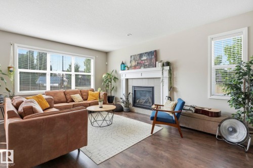 Expansive living area featuring large windows, wood-finish flooring, a tile-surround fireplace with a white mantel, and light-toned walls - 3204 Abbott Crescent Sw, Edmonton, AB - Indoor Photo Showing Living Room With Fireplace