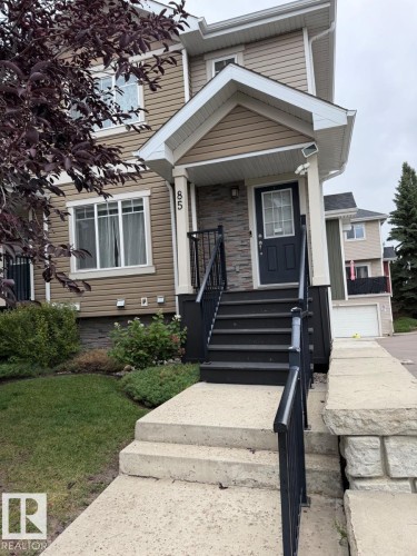Siding exterior with stone accents, covered entry, front porch with black railings, and concrete walkway - #85 9535 217 St Nw, Edmonton, AB 