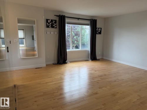 Bright interior space featuring wood-finish flooring, a large window, and light-toned walls - #85 9535 217 St Nw, Edmonton, AB 
