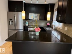 Kitchen featuring dark cabinetry, stainless steel appliances, dark stone countertops, a tiled backsplash, and pendant lighting - 