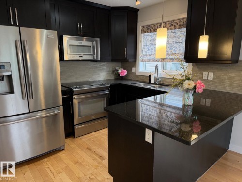 Kitchen featuring stainless steel appliances, dark cabinetry, light wood-finish flooring, dark countertops, and a tiled backsplash - #85 9535 217 St Nw, Edmonton, AB 