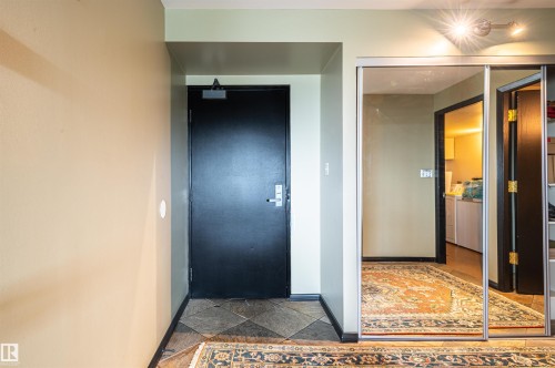 Tile flooring entrance with a dark door, mirrored sliding closet doors, and track lighting - #1202 10010 119 St Nw, Edmonton, AB 