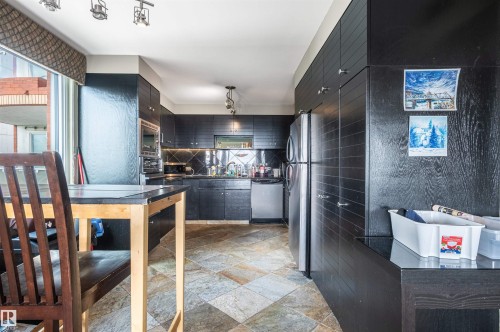 Slate tile flooring, dark wood-finish cabinetry, stainless steel appliances, and integrated kitchen lighting - #1202 10010 119 St Nw, Edmonton, AB 