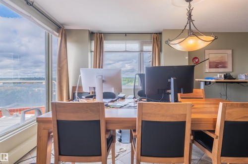 Spacious room featuring floor-to-ceiling windows, a large wood-finish table, a decorative semi-flush mount light fixture, and recessed lighting - #1202 10010 119 St Nw, Edmonton, AB 