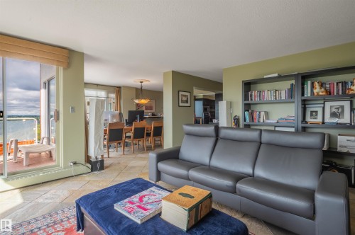Sliding glass doors leading to a balcony, tile flooring, built-in shelving, and a recessed dining area with a chandelier - #1202 10010 119 St Nw, Edmonton, AB 