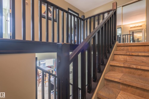 Wood-finish staircase with black railing and balusters, featuring a mirrored wall with a vanity light fixture - #1202 10010 119 St Nw, Edmonton, AB 
