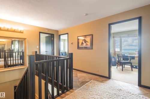 Hardwood staircase with black railings, framed doorways, wall-mounted light fixture, and tile flooring - #1202 10010 119 St Nw, Edmonton, AB 