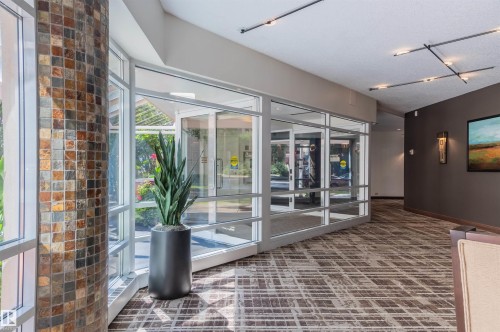 Floor-to-ceiling windows, patterned carpeting, natural stone tile column, recessed lighting, and wall sconces - #1202 10010 119 St Nw, Edmonton, AB 