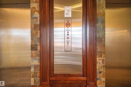 Stainless steel elevator doors framed by wood trim and varied stone tile accents - #1202 10010 119 St Nw, Edmonton, AB 