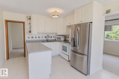Modern kitchen featuring white cabinetry, stainless steel appliances including a French-door refrigerator and electric range, quartz countertops, a central island with prep space, recessed ceiling lighting, and abundant natural light from multiple windows - 3911 117 Street Nw, Edmonton, AB 
