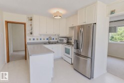 Modern kitchen featuring white cabinetry, stainless steel appliances including a French-door refrigerator and electric range, quartz countertops, a central island with prep space, recessed ceiling lighting, and abundant natural light from multiple windows - 
