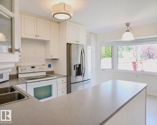 White cabinetry, stainless steel refrigerator, electric range, double basin sink, and a large bay window - 3911 117 Street Nw, Edmonton, AB 