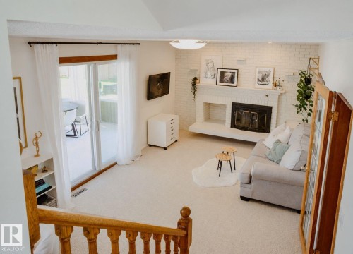 Spacious living area featuring a white painted brick fireplace, sliding glass door to exterior, light-toned carpeting, and a built-in shelving unit - 3911 117 Street Nw, Edmonton, AB 