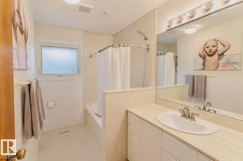 Bathroom featuring a built-in tub with shower, white wall tiling, frosted window, vanity with integrated sink, and a large wall mirror - 3911 117 Street Nw, Edmonton, AB 