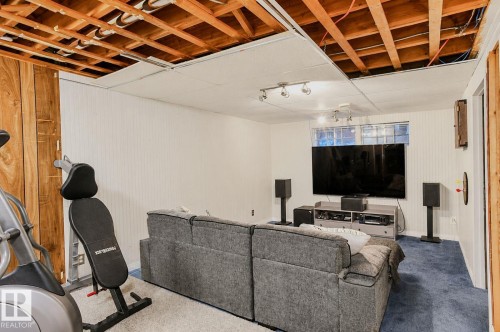 Exposed ceiling joists with partial drop ceiling panels, white beadboard-style wall paneling, and a window with glass block accents - 3911 117 Street Nw, Edmonton, AB 