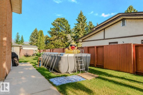 Expansive backyard featuring a manicured lawn, an above-ground pool with a ladder, wood fencing, and mature trees - 3911 117 Street Nw, Edmonton, AB 