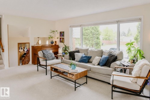 Large window with exterior landscaping, carpeted flooring, and a staircase with wood railing - 3911 117 Street Nw, Edmonton, AB 