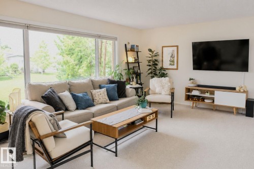 Expansive window wall with roller shades, light-toned wall paint, neutral carpet flooring, and a built-in media console - 3911 117 Street Nw, Edmonton, AB 