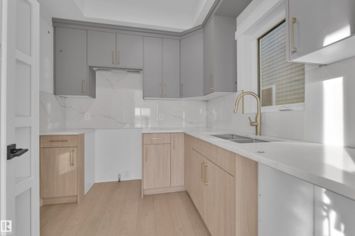 Kitchen featuring light gray upper cabinetry, natural wood-finish lower cabinetry, white countertops, a dual basin stainless steel sink, and a gold-tone gooseneck faucet - 226 Linden Loop, Leduc, AB 