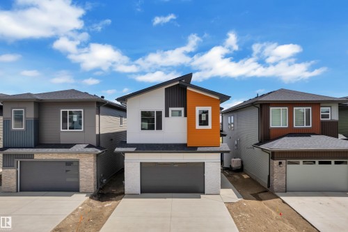 Modern exterior with a white, orange, and dark panel facade, featuring a prominent front-facing garage with a concrete driveway - 226 Linden Loop, Leduc, AB 