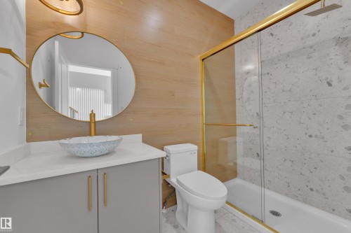 Modern vanity with a vessel sink, gold-finish fixtures, a gold-framed round mirror, and a shower with a sliding glass door - 226 Linden Loop, Leduc, AB 