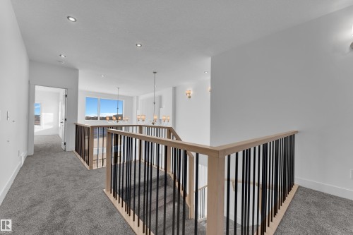 Modern staircase with light wood railings and black metal balusters, recessed ceiling lighting, wall sconces, and neutral carpeting - 226 Linden Loop, Leduc, AB 