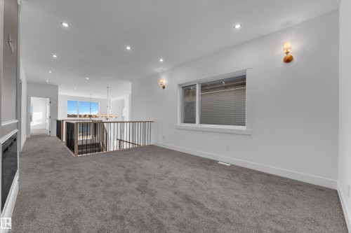Recessed lighting, wall sconces, carpet flooring, a built-in fireplace, and a light wood-finish and black metal railing system - 226 Linden Loop, Leduc, AB 
